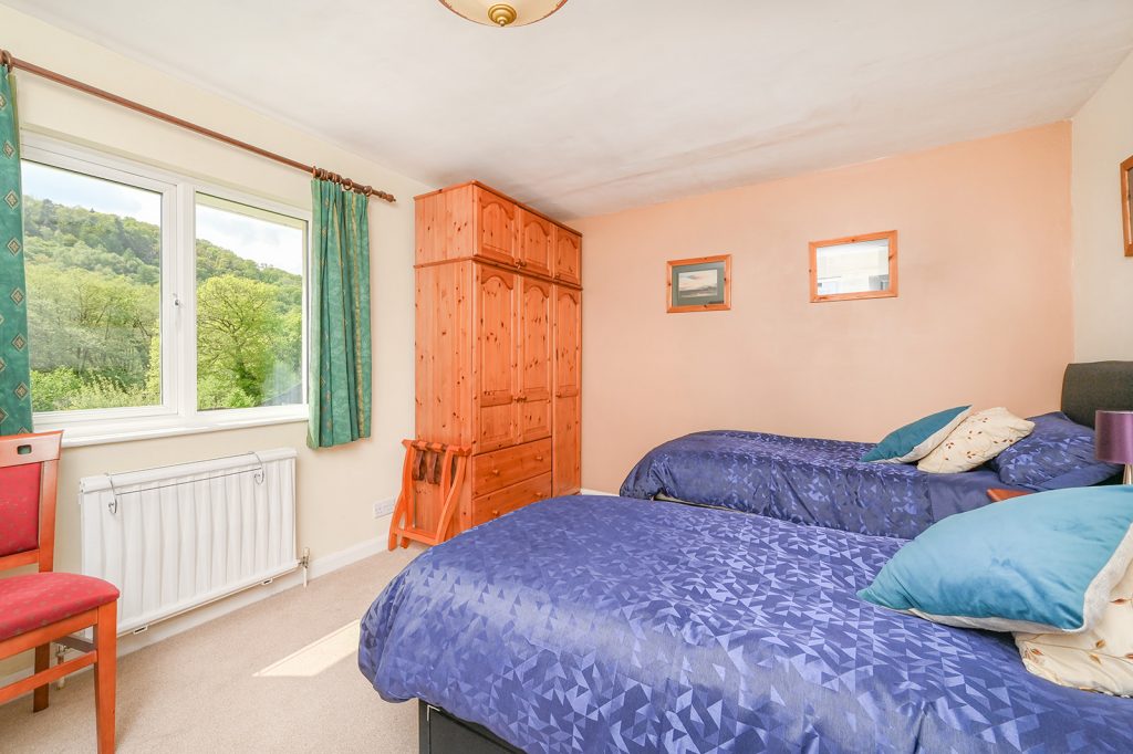 Twin beds in Double Room with blue duvet covers. View of garden through window and triple pine wardrobe