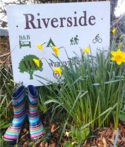 Riverside street sign with a pair of striped wellies and daffodils. First image in March Newsletter