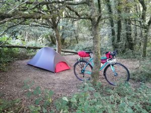 bicycle leaning against a tree with small bike packing tent in background on Charcoal pitch under the trees