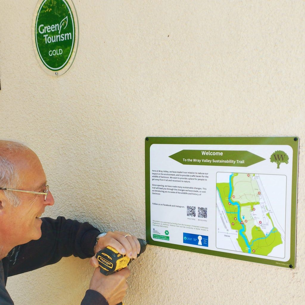 Kevin screwing the Welcome Board in place at the side of the house using a power screwdriver